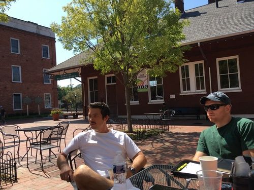 two men sitting at an outdoor table with Bibles and coffee